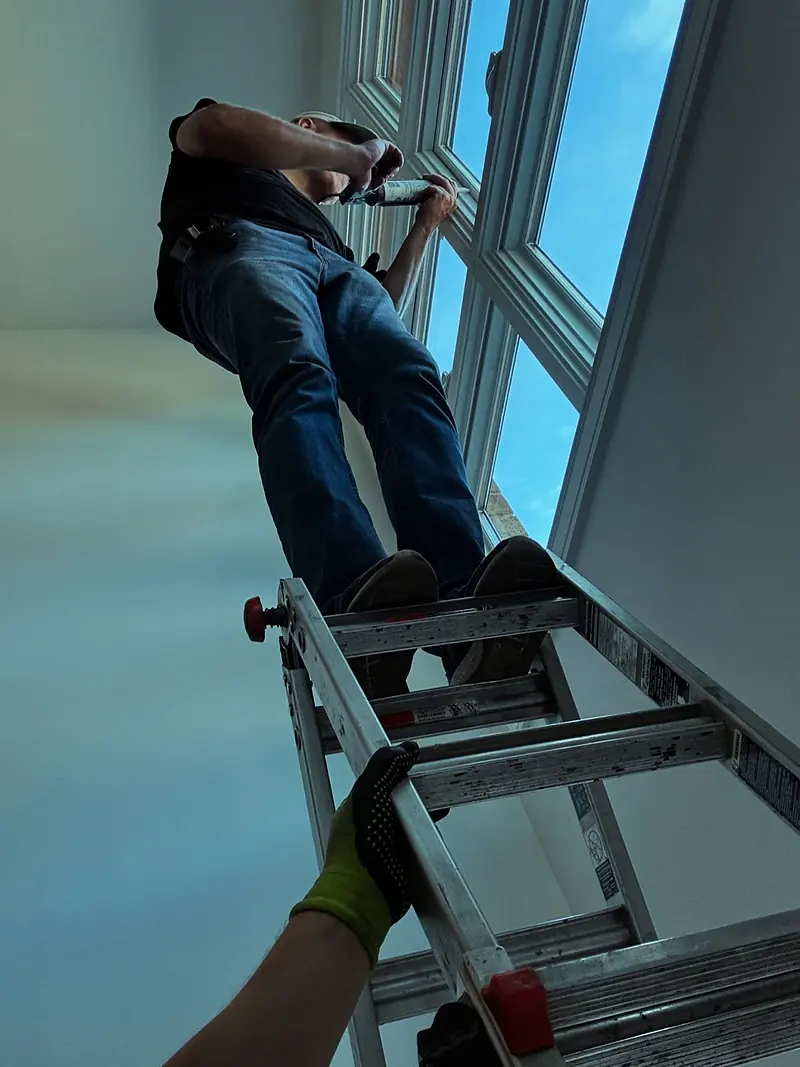 Our technician on a ladder working on a tall two-story window