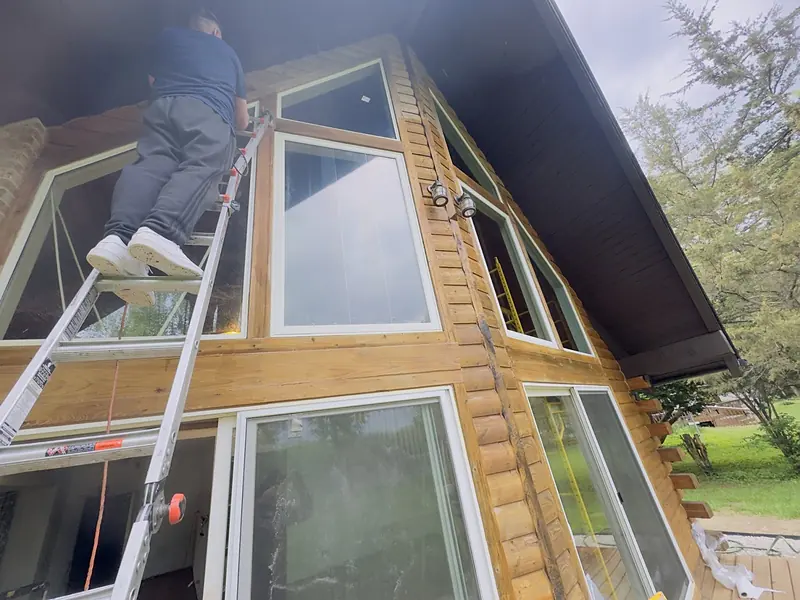 Our technician on a ladder replacing glass high on the two-story window wall of a log home