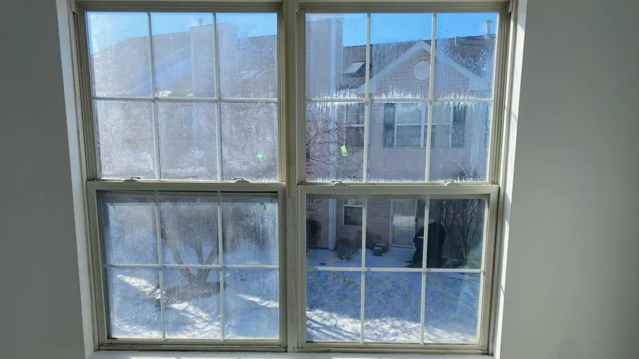 Double-hung windows with fog and mineral streaks between the panes in winter